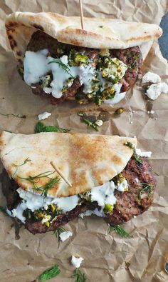 two pita sandwiches on wax paper with herbs and yogurt drizzled on top