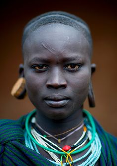 an african woman with dark skin and necklaces on her neck is looking at the camera