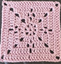 a pink crocheted square with black dots on it, sitting on a gray surface