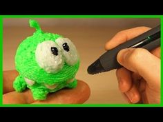 a hand holding a pen next to a green and white toy with eyes on it