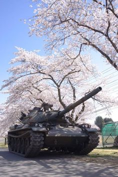 an old tank is parked on the side of the road in front of cherry blossom trees