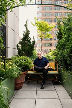 an older man sitting on a bench in the middle of a garden with potted plants