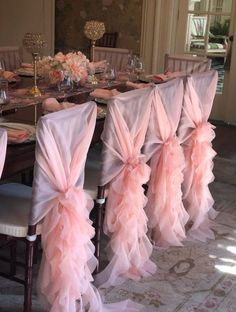 a dining room table with chairs covered in pink ruffled sashes and place settings