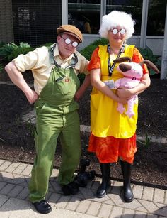 two people in costumes standing next to each other on a sidewalk, one holding a stuffed animal and the other wearing overalls