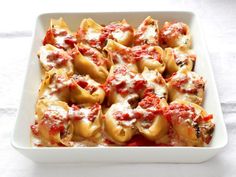 a white casserole dish filled with shells covered in marinara sauce and cheese