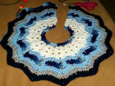 a crocheted blue and white doily with scissors on the table next to it