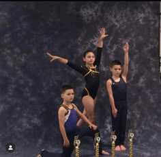 three young boys standing in front of a wall with their hands up and one boy holding his arms out