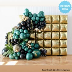 a table topped with chocolates and balloons in front of a gold box filled with green balls