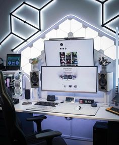 a computer desk with speakers, keyboard and monitor on it in front of a large screen