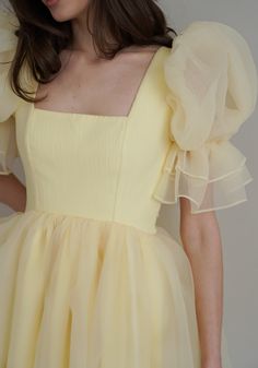 Introducing the Britney Dress in a delightful light yellow: a stunning creation crafted from delicate bubble organza. This lightweight dress features an elegant silhouette with a voluminous floating skirt that moves gracefully with every step. The charming puff sleeves add a whimsical touch, making it perfect for any special occasion. The Britney Dress is enclosed with delicate bow ties down the back, adding a romantic and feminine detail that completes the look. In light yellow, this dress exud Yellow Dress Puffy Sleeves, Ruffles Sleeves Dress, Womens Frocks Design, Sleeves Design For Frocks, Marriage Function Dresses For Women, Organza Dress Styles, Organza Sleeves Design, Yellow Dress With Sleeves, Yellow Dress Design