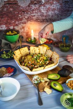 a table topped with plates and bowls filled with food next to a lit candle on top of a wooden cutting board