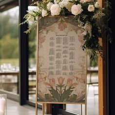 a sign with flowers and greenery on it next to a glass vase filled with candles