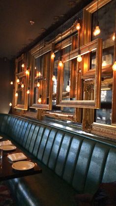 an empty restaurant with green booths and gold framed mirrors on the wall, along with place settings for dinner