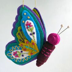 a colorful butterfly ornament hanging from a string with two knitting needles in front of it