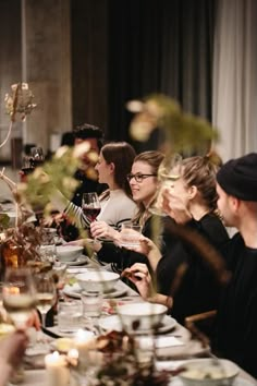 a group of people sitting at a long table with plates and wine glasses on it