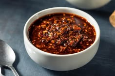 a white bowl filled with chili sauce next to a spoon and bread on a table