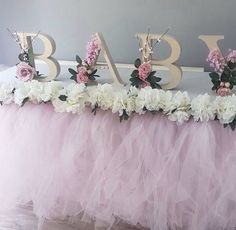 a pink tulle skirted table with flowers and letters that spell baby on it