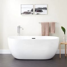 a white bath tub sitting in a bathroom next to a wooden table and two pictures on the wall