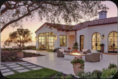 a patio with chairs and fire pit in front of a house at sunset or dawn