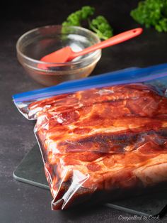 a piece of meat wrapped in plastic sitting on top of a counter next to a bowl