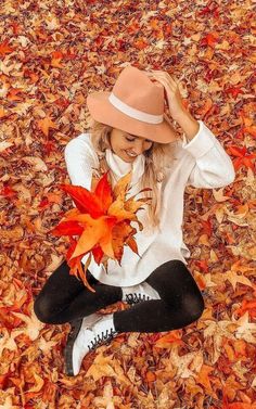 a woman sitting on the ground with leaves in front of her and wearing a hat