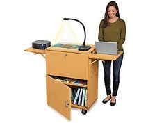 a woman standing next to a desk with a laptop on it