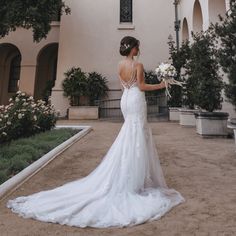 a woman standing in front of a building holding a white bouquet and wearing a wedding dress