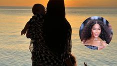 a woman holding a baby in her arms near the ocean with an orange sunset behind her