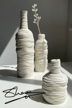 three white vases sitting next to each other on a table with a plant in the middle