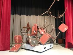 a pile of chairs sitting on top of a white platform in front of a red curtain