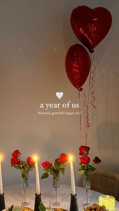 a table topped with plates and candles next to red heart shaped balloons in vases