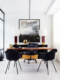 an office with black chairs and a large painting hanging on the wall above it's desk