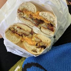 two sandwiches with bacon and cheese in paper wrappers on a person's lap