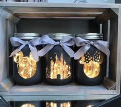 three mason jars with lights in them are sitting on a shelf, one has a castle and the other is a castle