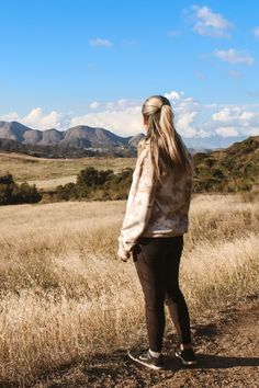 a woman standing on top of a dirt road in the middle of a dry grass field