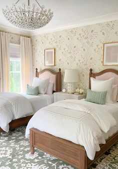 two twin beds in a bedroom with floral wallpaper and chandelier above them