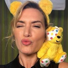 a woman holding a yellow teddy bear in front of her face and making a funny face