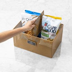 a person's hand reaching into a brown basket filled with cereals and snacks