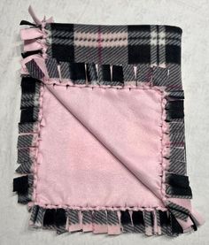 a pink and black plaid blanket with fringes on the edges, laying on a white surface