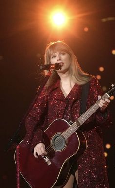 a woman holding a guitar while standing on top of a stage