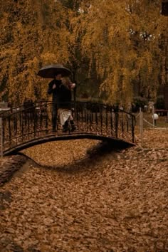 a person holding an umbrella standing on a bridge in the fall with leaves all around