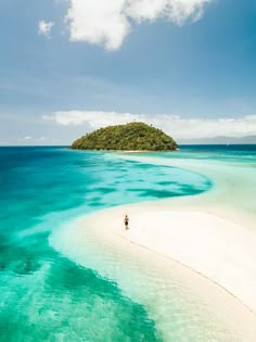 an island in the middle of blue water with a lone person standing on top of it