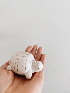 a hand holding a small ceramic turtle in it's left palm, against a white background