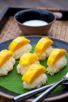 four pieces of mango on top of rice with sauce and spoons next to it