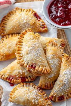 cranberry hand pies with powdered sugar on top and sauce in the background