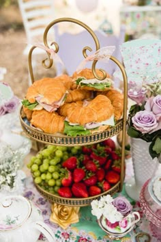 three tiered trays filled with sandwiches and fruit on top of a floral table cloth