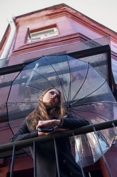 a woman holding an open umbrella on top of a metal railing next to a red building