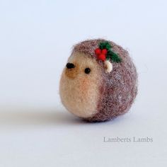 a needle - felt hedge with a red bow on it's head, sitting in front of a white background