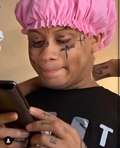 a woman with tattoos on her face looking at a cell phone while wearing a pink hat