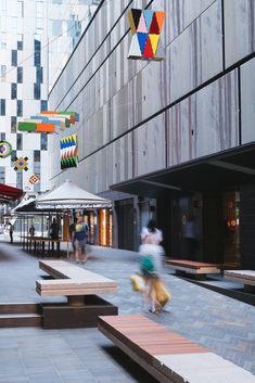 people are walking down the street in front of some buildings with umbrellas and benches